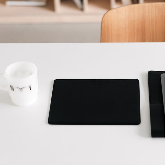 Labovarde Mouse Pad in Black — Perspective view of the mouse pad on a white desk next to a white mug