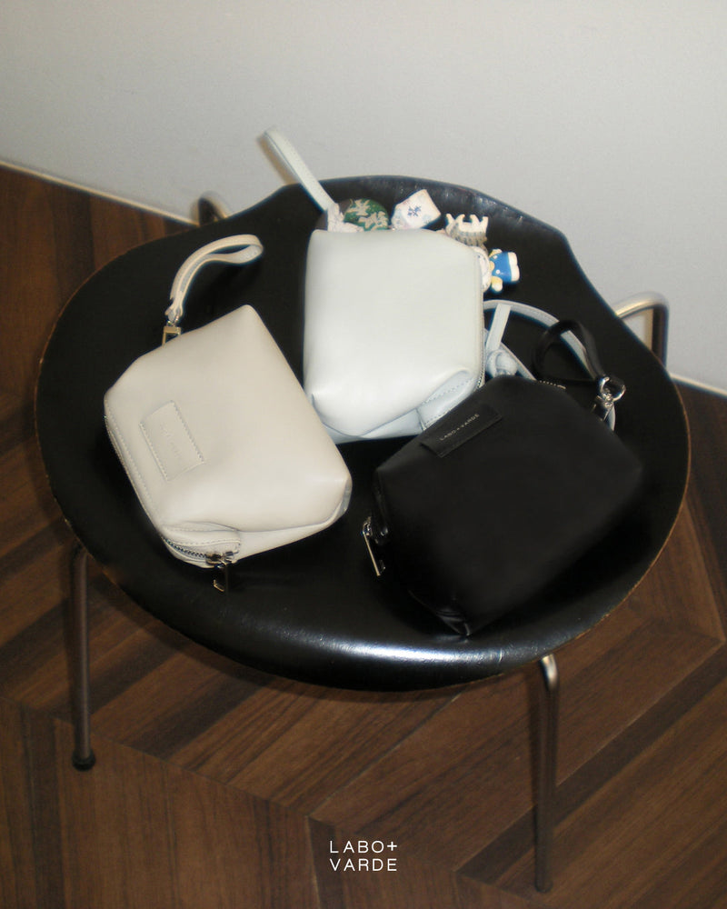Three small Labovarde Shell Pouch Bags on a black table. The central pouch has many character charms.