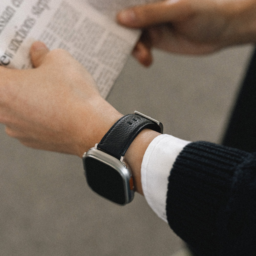 Labovarde Apple Watch Band in Black — Close-up view of a wrist wearing an Apple Watch while holding a newspaper