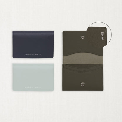 Labovarde Business Card Holder — Flat lay view of closed navy and clear blue cases next to an open etoupe holder showing custom engraving detail on a white background