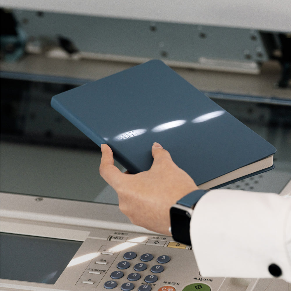 Labovarde Business Diary in Pale-Blue — Close-up view of a hand holding the closed diary over an office copier
