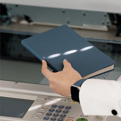 Labovarde Business Diary in Pale-Blue — Close-up view of a hand holding the closed diary over an office copier