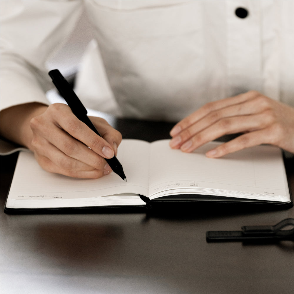 Labovarde Business Diary in Black — Close-up view of hands writing with a black pen in the open diary