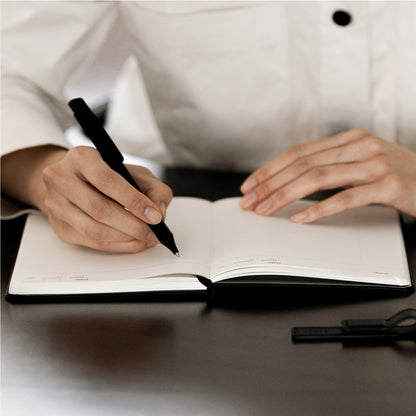 Labovarde Business Diary in Black — Close-up view of hands writing with a black pen in the open diary