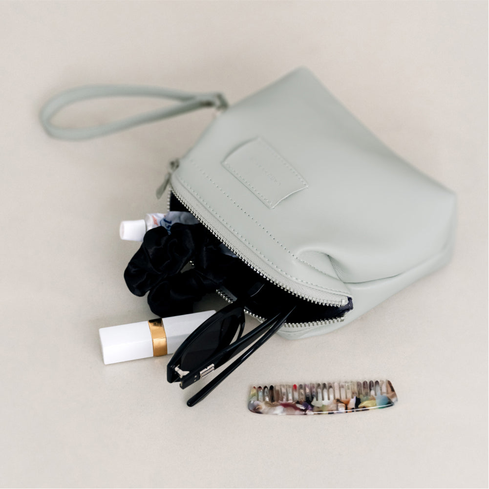 Labovarde Shell Pouch Bag in Clear-Blue — Top view of the open bag with sunglasses, lipstick, and a comb spilling out